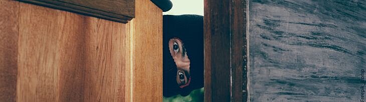 Einbrecher schaut durch Tür