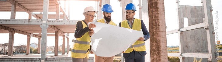 Drei Bauexperten mit Bauplan auf Baustelle