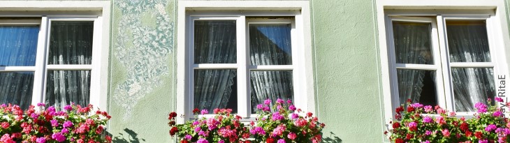 Drei Fenster mit rosaroten Geranien