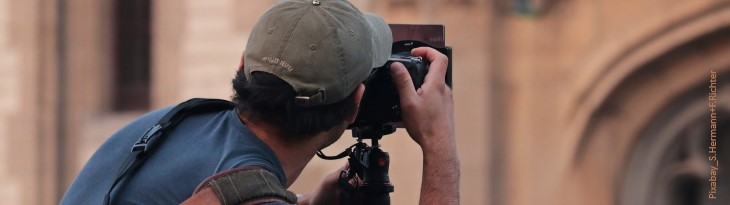 Mann mit Kappe und blauem T-Shirt fotografiert Kirche im Hintergrund