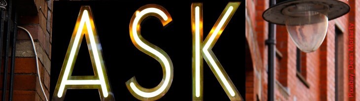 Schild beschriftet mit "Ask" in Neonlicht an verlinkerter Häuserfassade 