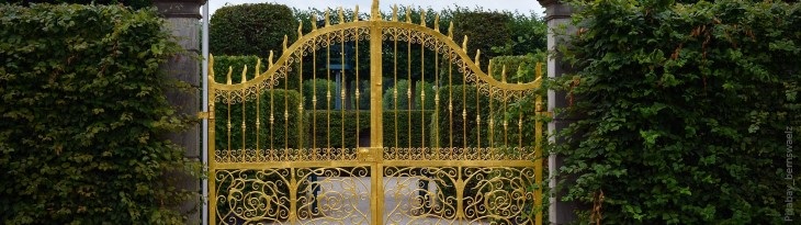 goldenes Tor zwischen Säulen und grünen Hecken