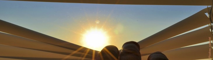 Blick durch mit Fingern heruntergedrückte Jalouse in die Sonne