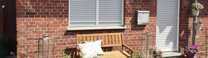 mit Rolläden verschattete Fenster und Tür in roter Ziegelfassade